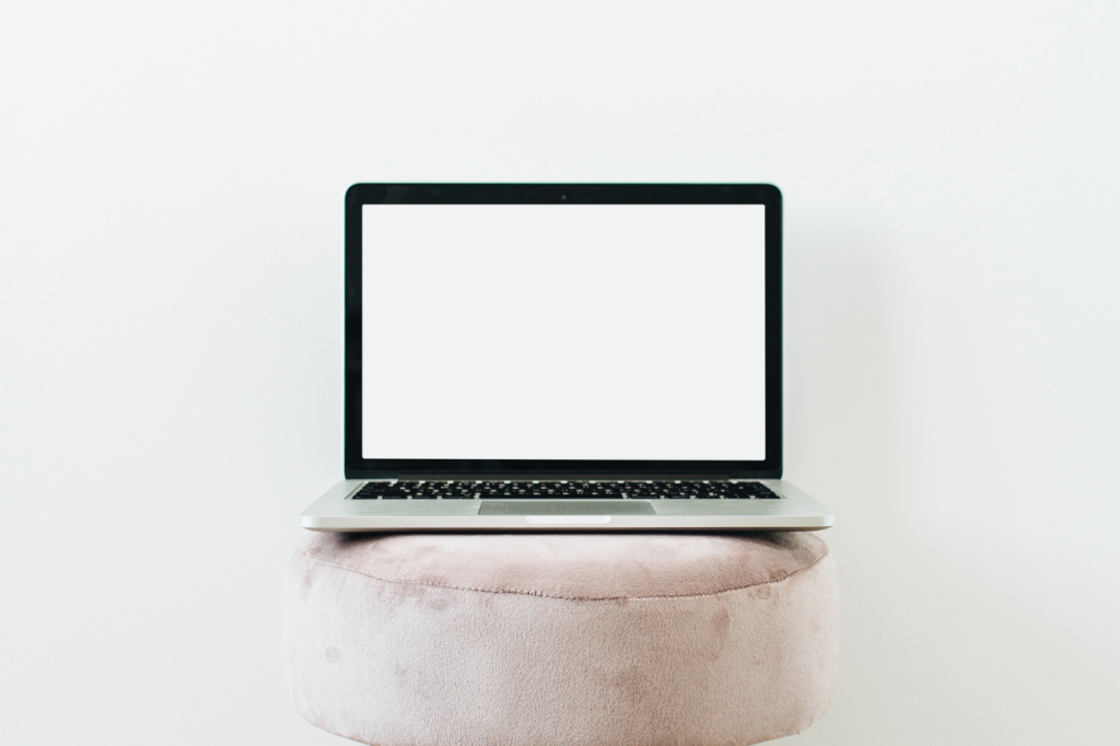 Blank laptop sits on round white cushion against a white background